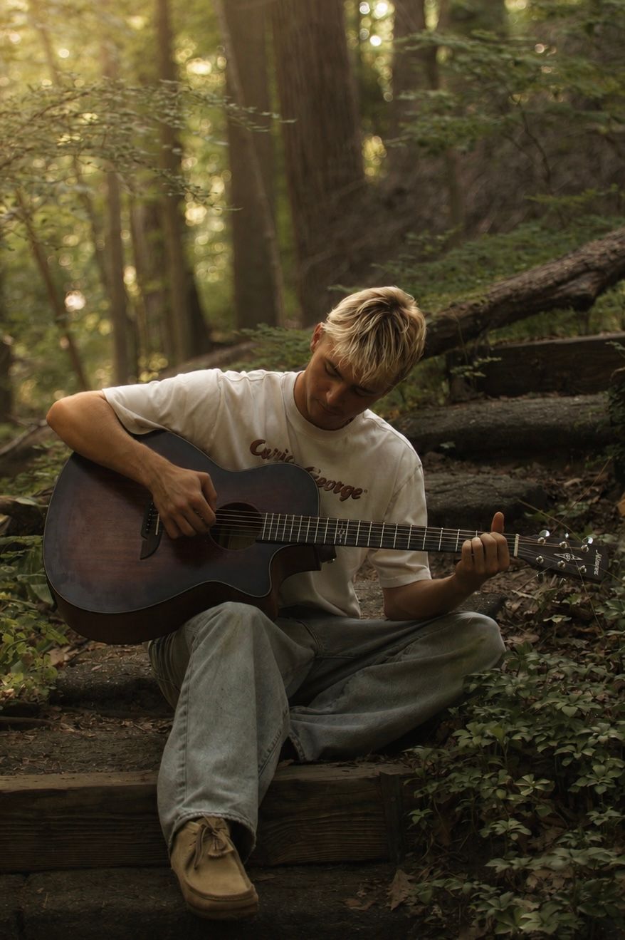 A guitarist seated on woodland steps.